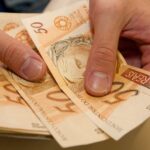 mãos segurando notas de cinquenta reais auxílio emergencial renda mínima crédito