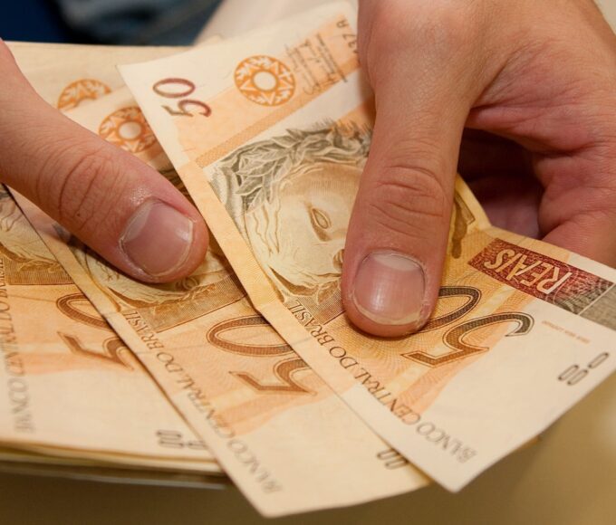 mãos segurando notas de cinquenta reais auxílio emergencial renda mínima crédito