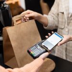 Imagem mostra pessoa usando o smartphone para pagar comprar; comércio, varejo